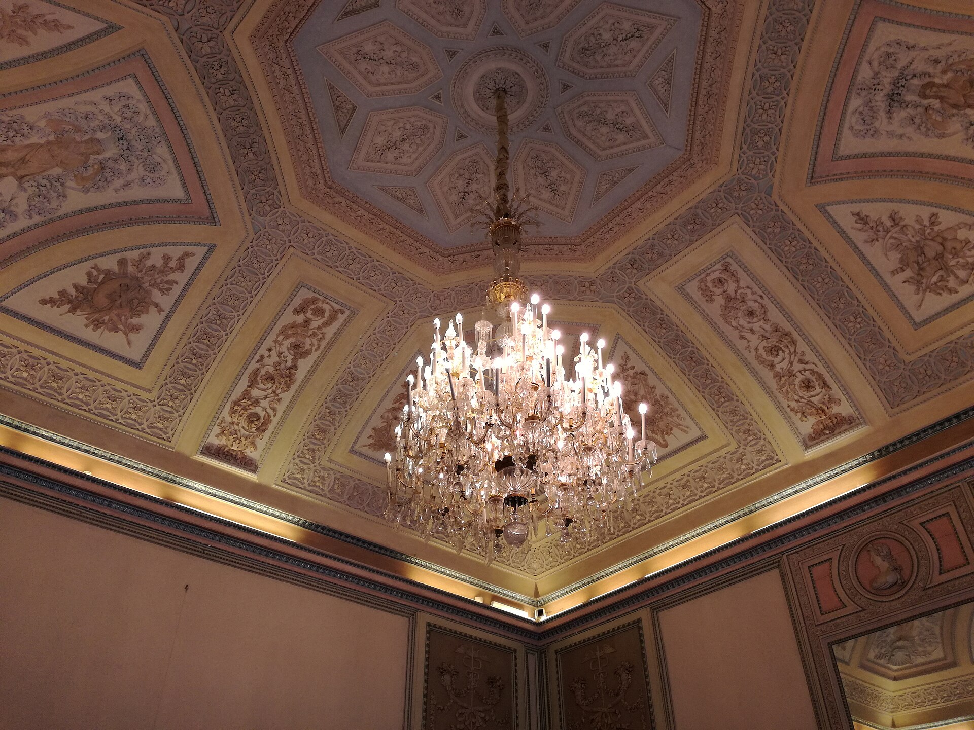 The ceiling of a hall with rich stucco decoration: cornices, panels, festoons and reliefs framing the painted compartments