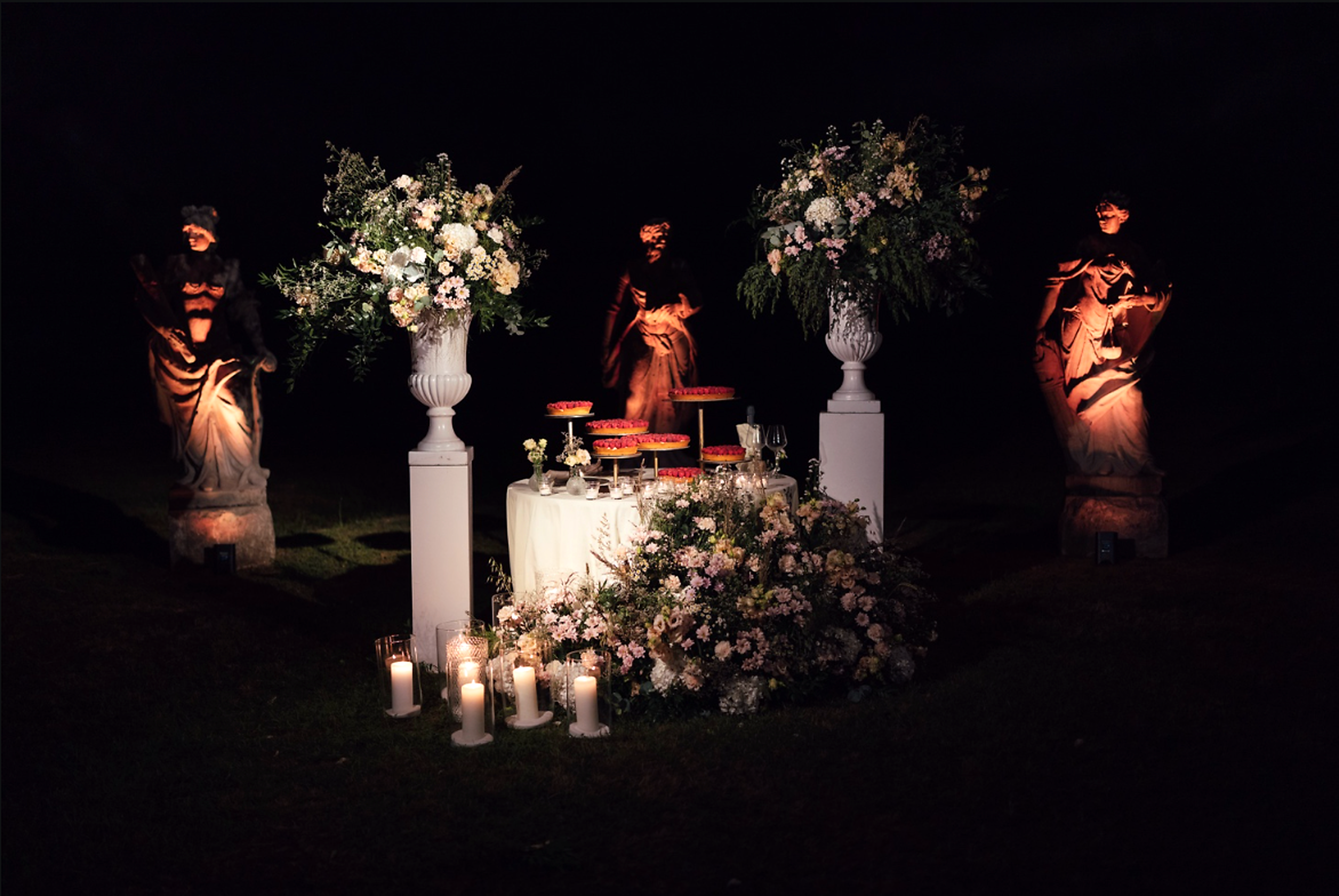 Evening setup in the villa's park, with lit statues, floral arrangements and candles