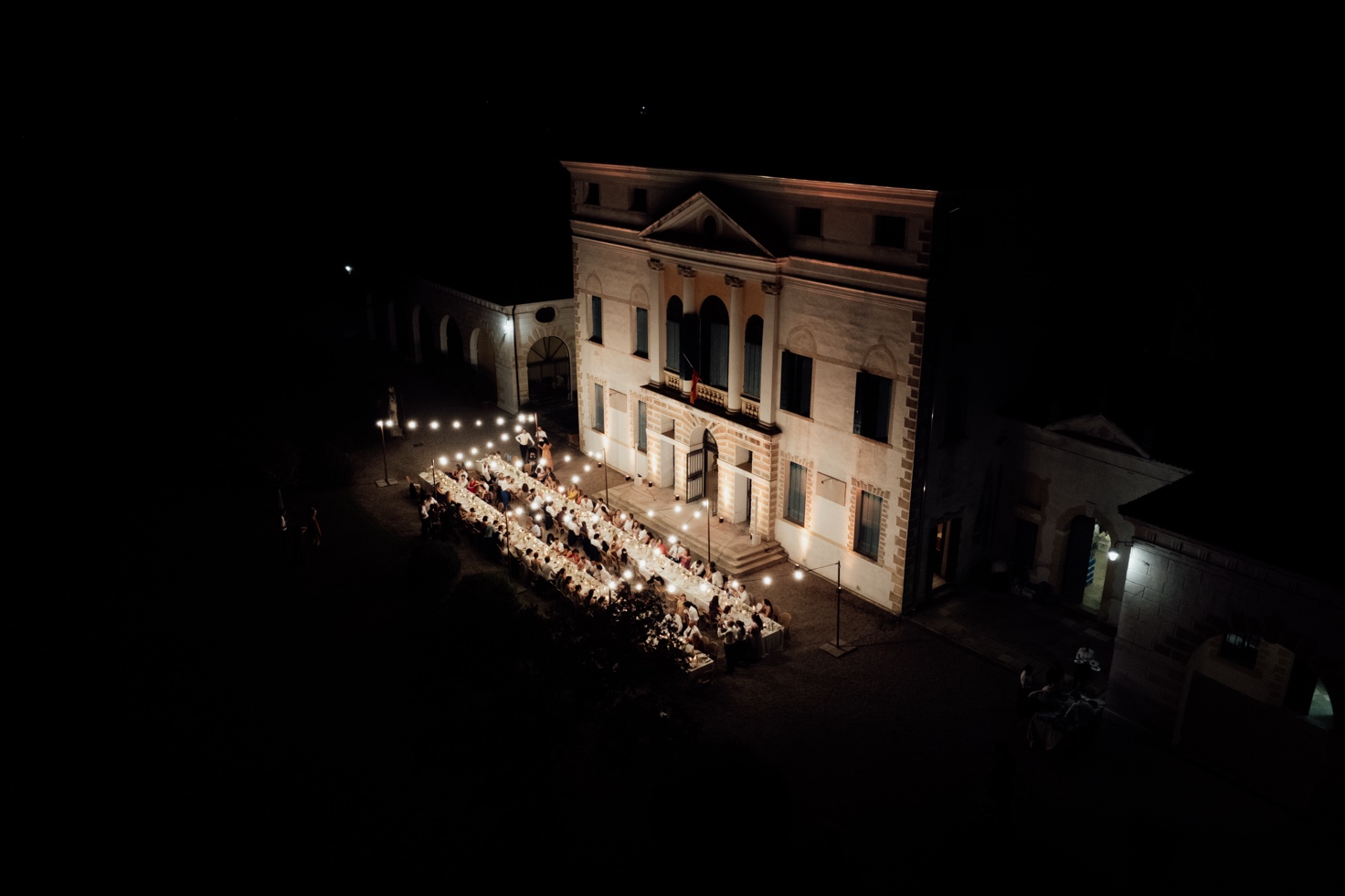 Evening gala dinner in front of the lit façade of Villa Loredan, with a single long table and suspended lights