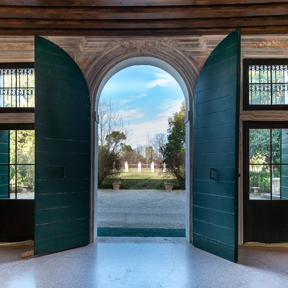 The villa's manorial door open onto the park, between green shutters and garden statues